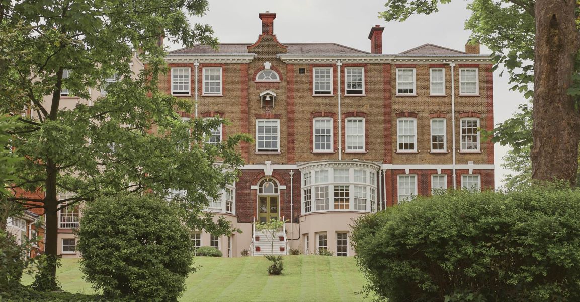 St Ursula Convent School - A large, red brick building with many windows stands on a green lawn, partially obscured by trees